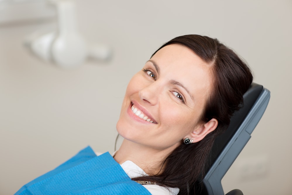 A woman smiles while sitting in a dental chair, highlighting the importance of proper dental checkups.