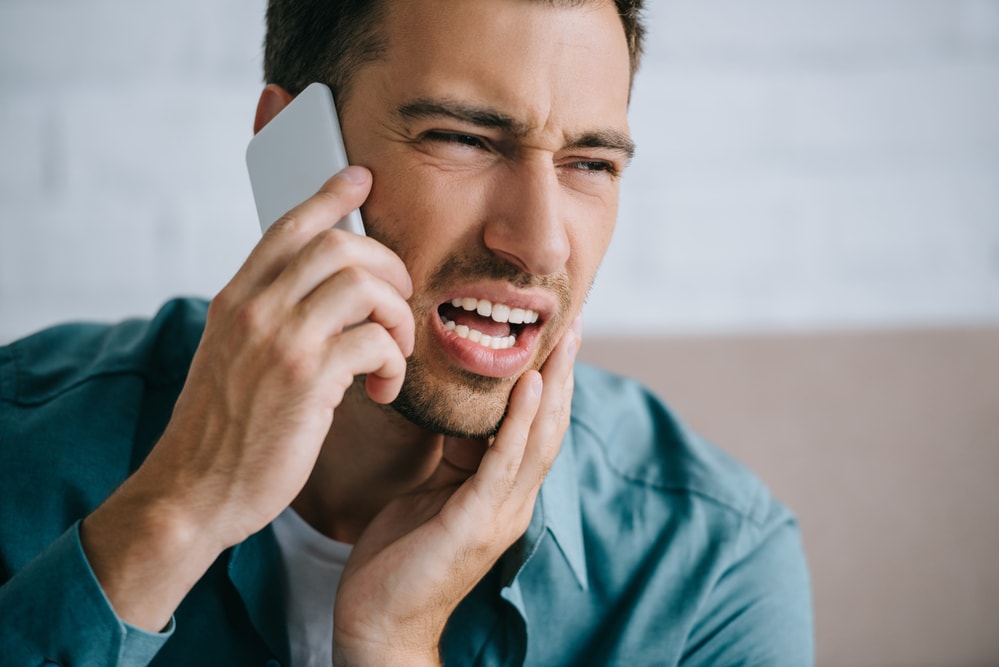 A man experiencing a dental emergency while talking on a cell phone with his mouth open.