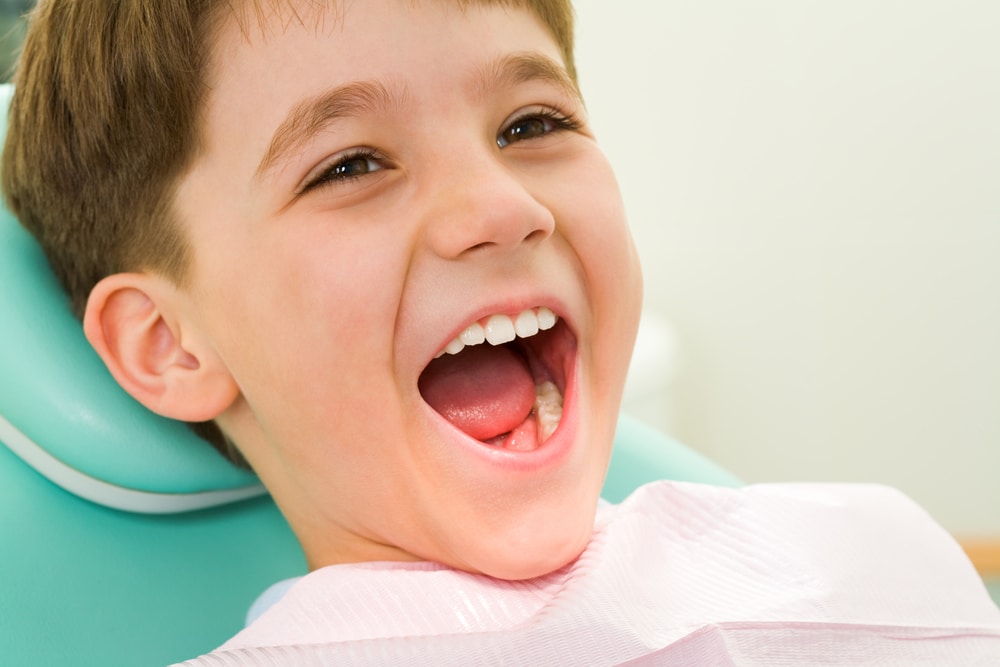 A young boy is sitting in a dental chair, experiencing common dental problems in kids, with his mouth open.